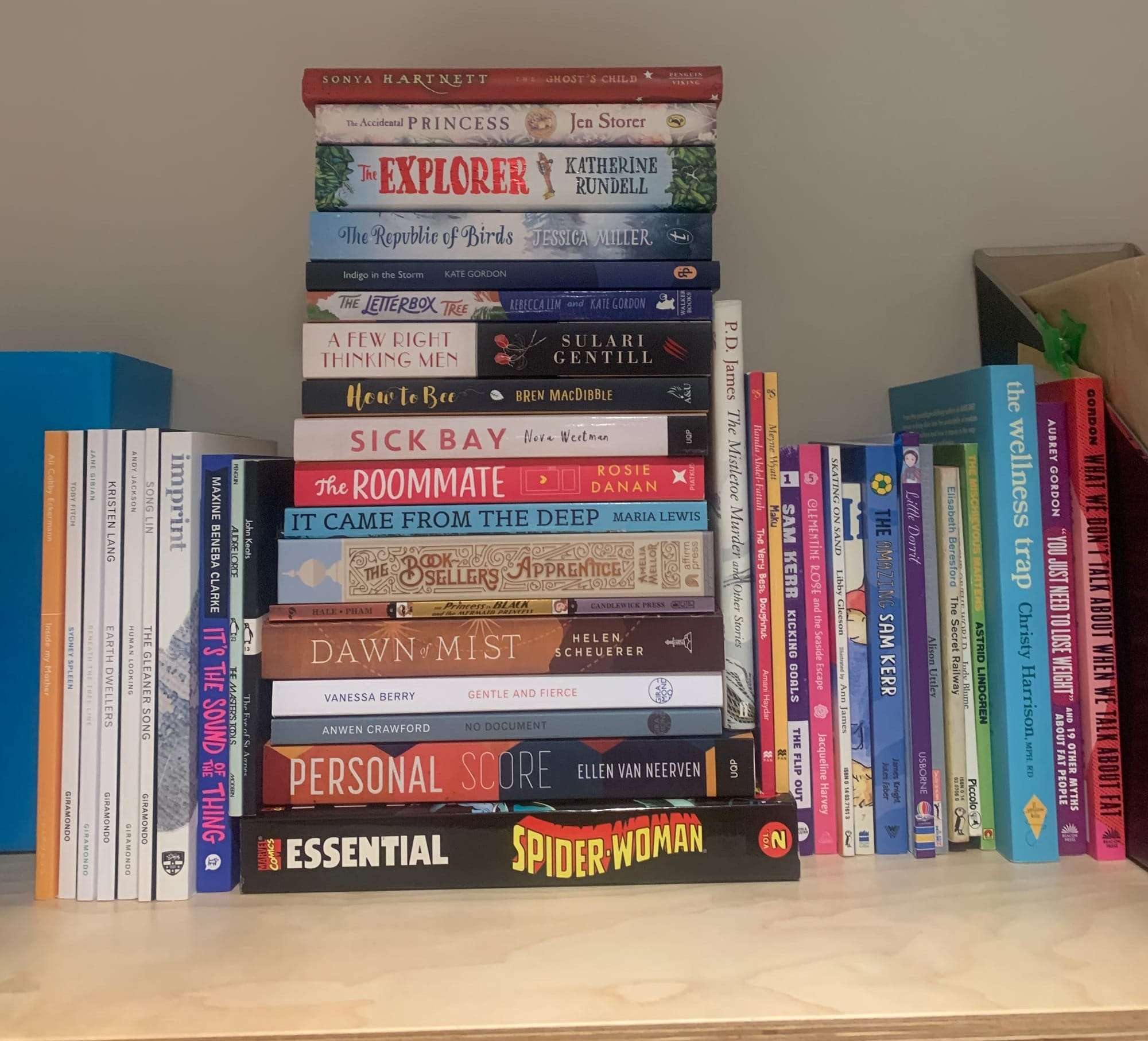 A stack of 65 books on a wooden shelf, most a fairly skinny but some are not.